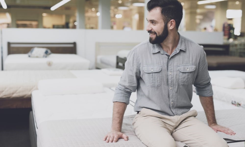 A man smiles sitting on the mattress in a mattress store